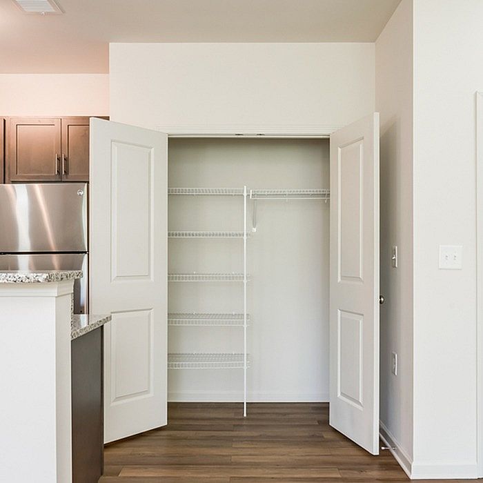 Bright and spacious walk-in closet with sleek sliding doors, featuring modern shelving against a backdrop of elegant wood flooring and adjacent to a stylish kitchen area.