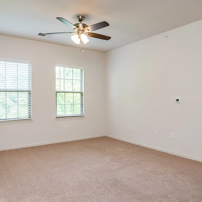 Bright, spacious room with soft carpeting, large windows, and a modern ceiling fan, ideal for a cozy bedroom.