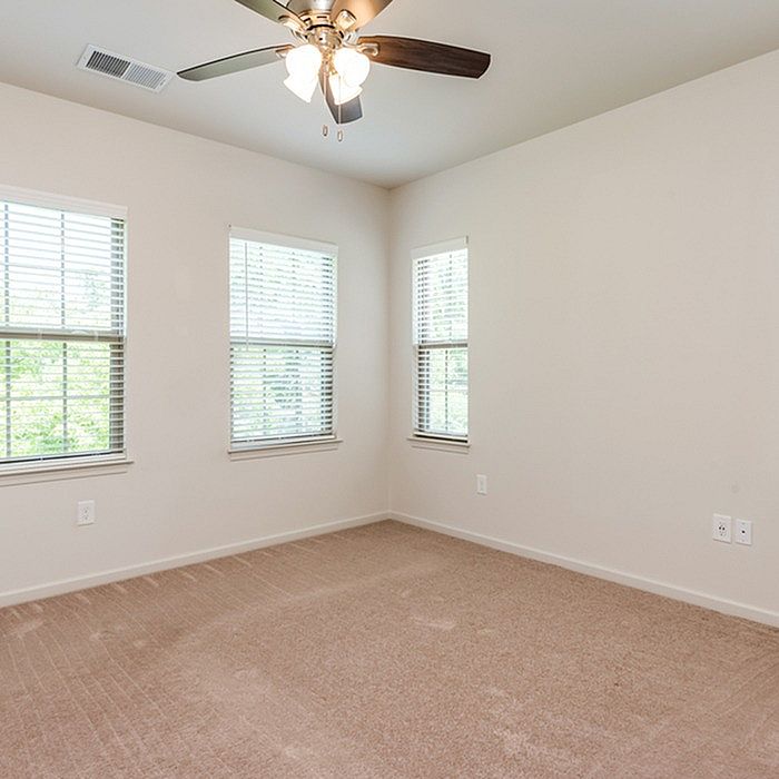 Bright and airy room with plush carpeting and large windows, enhanced by a modern ceiling fan.