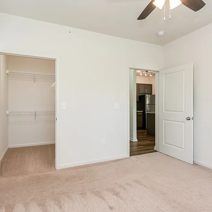 Modern bedroom with walk-in closet and view into a sleek kitchen with stainless steel appliances, offering a blend of comfort and style.