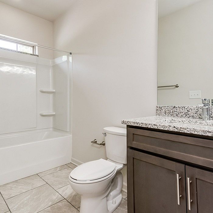 Modern bathroom with elegant granite countertop, sleek cabinetry, and a spacious bathtub with glass enclosure.