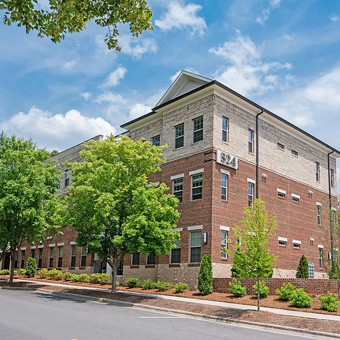 Charming brick apartment building with elegant architectural details, surrounded by lush greenery under a bright blue sky.