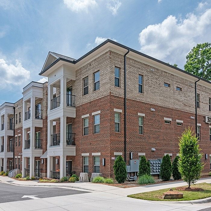 Elegant brick apartment building with classic balconies and lush landscaping, bathed in natural sunlight.