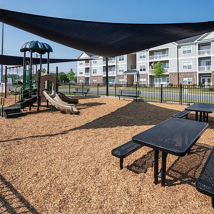 Inviting outdoor playground and picnic area with modern apartment buildings in the background, perfect for family living.