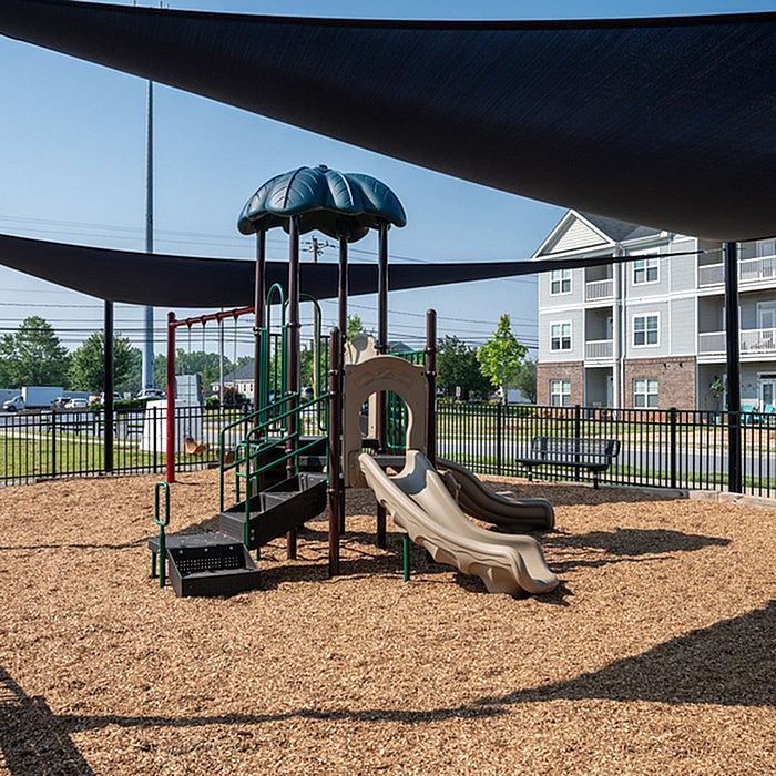 Inviting outdoor playground with modern slides and climbing structure, shaded by elegant canopies, located near charming apartment buildings.
