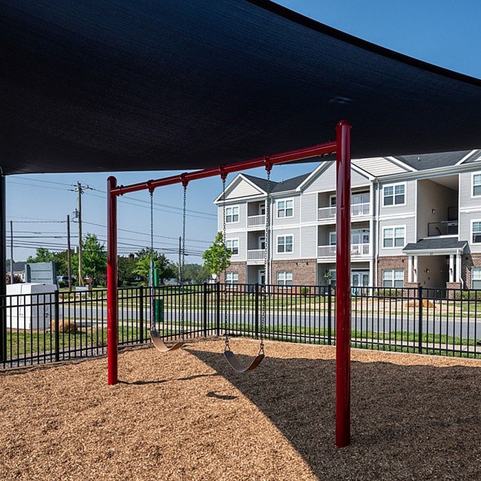 Inviting modern apartment complex with a charming playground featuring swings and a shaded area, perfect for family-friendly living.