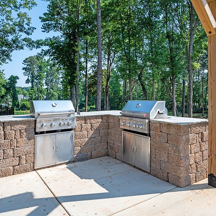 Charming outdoor patio with pergola, featuring picnic tables and a barbecue grill, set against a lush green backdrop.