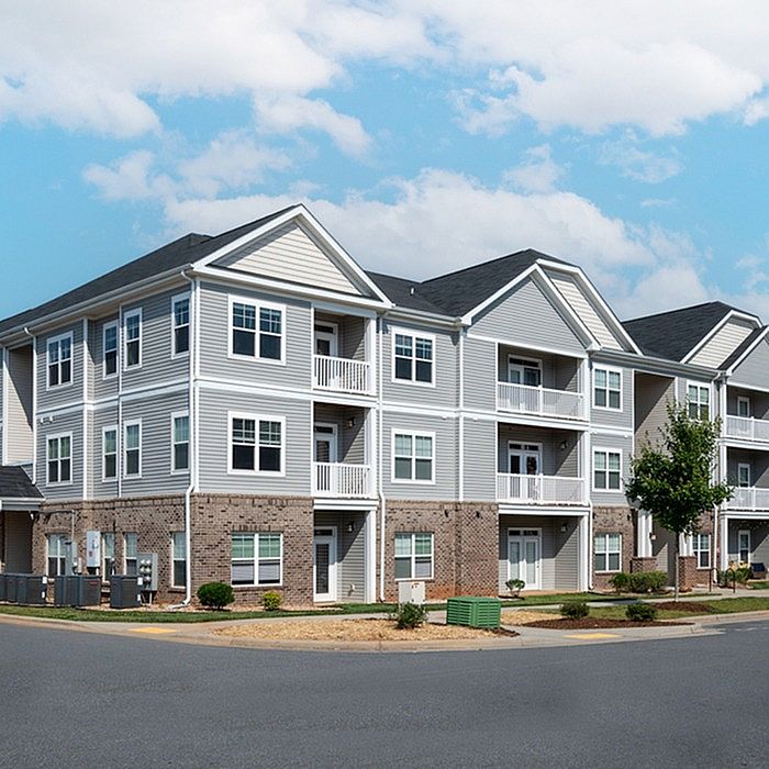 Modern three-story apartment building with elegant balconies, surrounded by lush greenery and spacious parking.