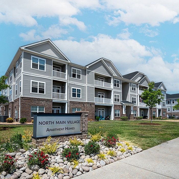 Charming North Main Village apartment homes with modern architecture, landscaped gardens, and inviting balconies under a clear blue sky.