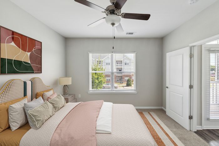 Inviting bedroom with chic decor, featuring a modern ceiling fan, large window with a view, and stylish artwork.