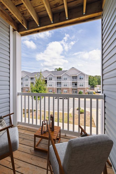 Inviting balcony view from a charming apartment, featuring cozy seating and scenic outlooks over a modern residential complex against a bright, blue sky.