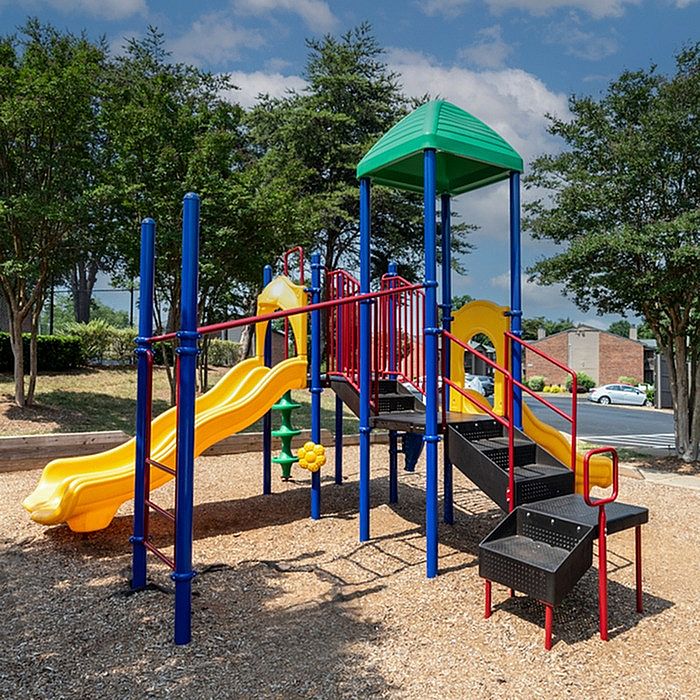 Vibrant playground with colorful slides and climbing structures surrounded by lush trees, perfect for family fun and outdoor adventures.