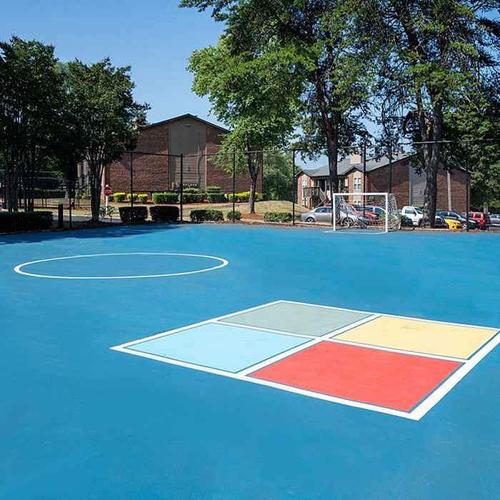 Vibrant outdoor recreational area with a bright blue sports court surrounded by lush greenery and modern apartment buildings, offering a perfect blend of active living and serene environment.