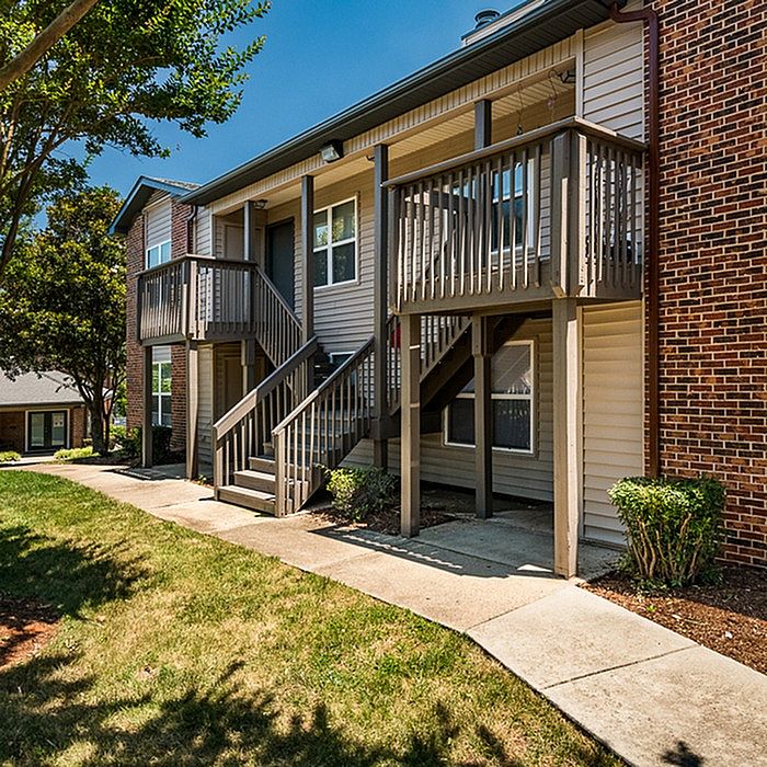 Charming two-story apartment building with private balconies, set amidst lush greenery and sunny pathways.
