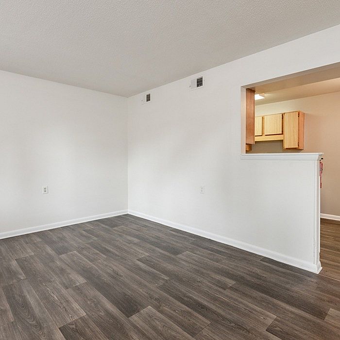 Bright open living space with sleek hardwood floors and an adjacent kitchen, ideal for modern living.