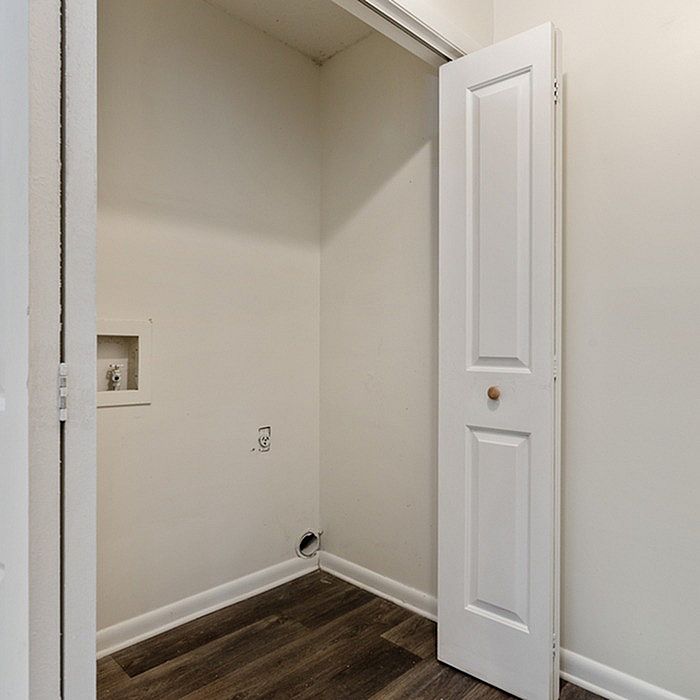 Practical laundry nook with stylish white folding door and elegant dark wood flooring.