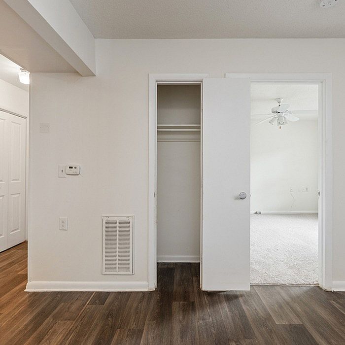 Inviting apartment showcasing a walk-in closet, elegant wooden flooring, and a light-filled room with ceiling fan in the background.