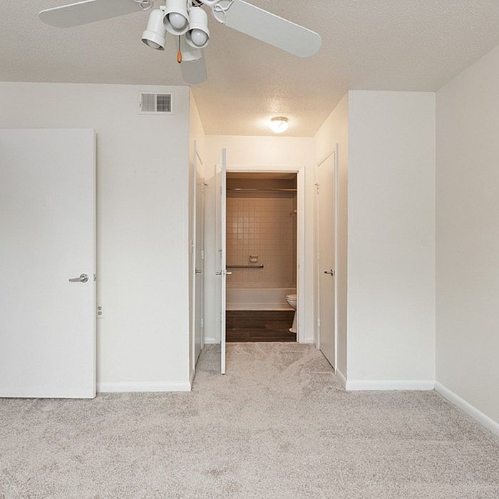 Bright and inviting bedroom with plush carpet and ceiling fan leading to a private, modern bathroom.