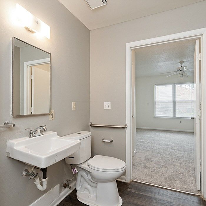 Bright, modern bathroom featuring sleek fixtures, a large mirror, and a view into a sunlit room with plush carpeting.