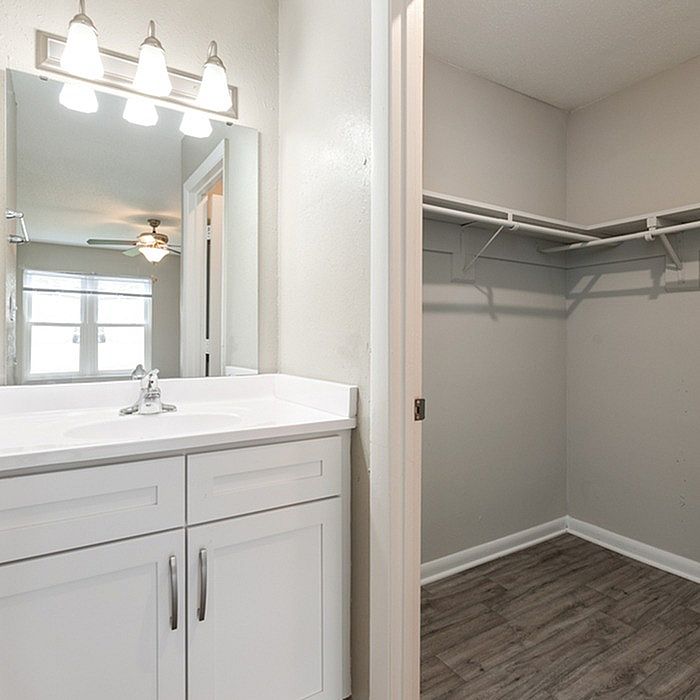 Bright bathroom with a sleek white vanity and a spacious walk-in closet, featuring elegant lighting and modern finishes.