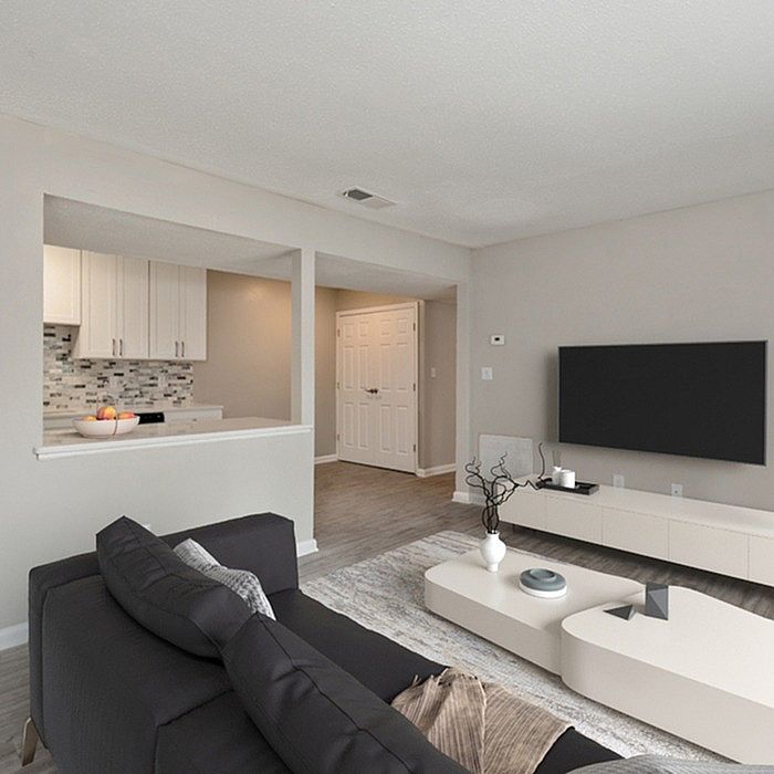 Modern living room with sleek furniture, open-concept layout, and adjacent kitchen featuring stylish backsplash.
