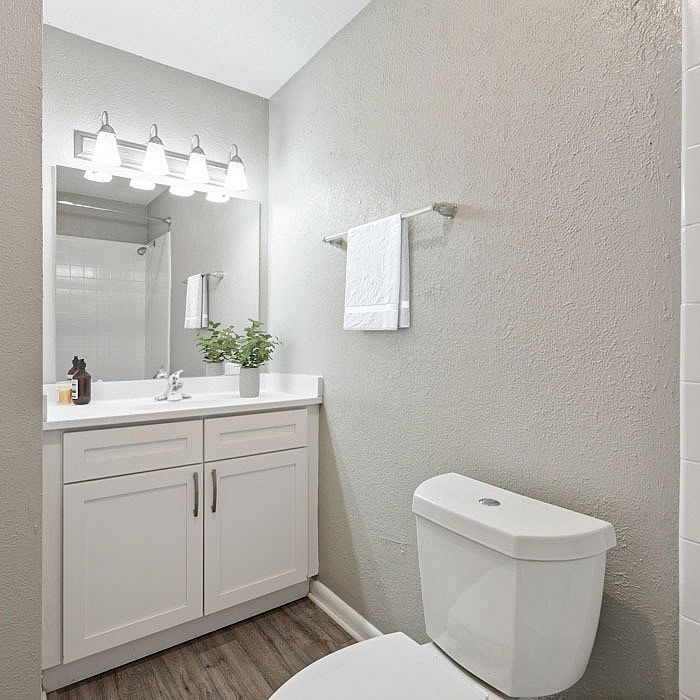 Elegant bathroom featuring a sleek vanity with bright lighting, contemporary fixtures, and a modern white toilet set against a soothing gray wall.