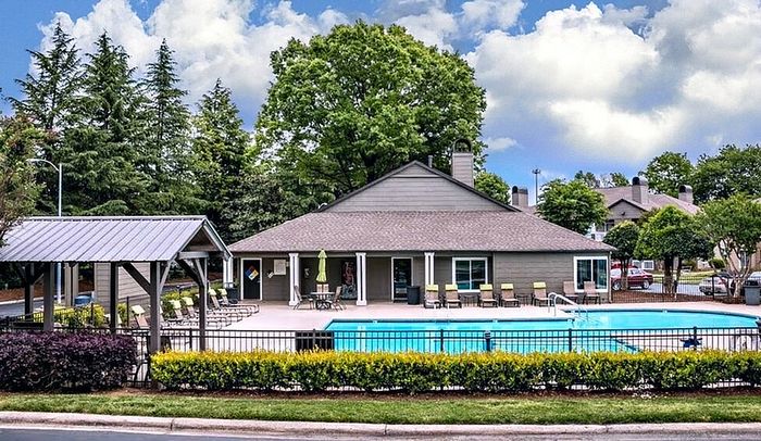 Inviting apartment community with a sparkling pool, ample seating, and lush greenery, perfect for relaxation and leisure.