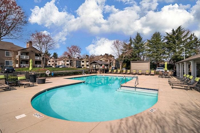 Inviting outdoor pool area surrounded by lush greenery and stylish apartment buildings, perfect for relaxation and leisure.