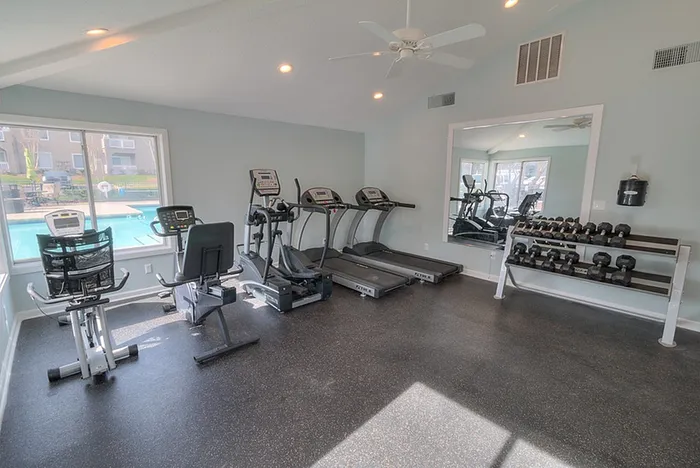 Bright and modern fitness room with treadmills, exercise bike, and free weights, overlooking a sparkling outdoor pool.