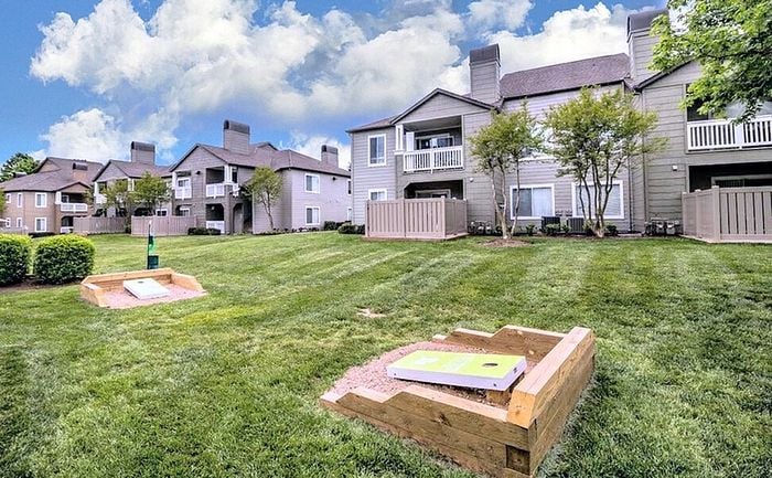 Charming apartment complex with beautiful landscaped grounds, highlighting a unique outdoor entertainment area and spacious, modern balconies set against a vibrant blue sky.