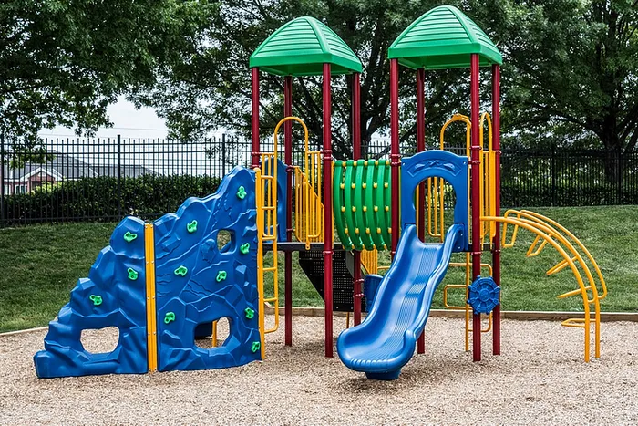 Vibrant playground with colorful climbing wall, slide, and tunnels set amidst lush greenery.