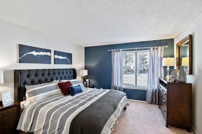 Inviting bedroom with a plush tufted headboard, stylish bedding, and a sunlit window offering serene views.