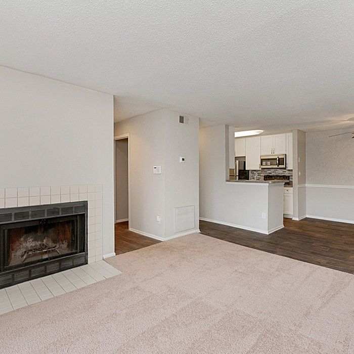 Inviting apartment interior with a cozy fireplace, plush carpeting, and an open kitchen layout featuring modern appliances, perfect for comfortable living.