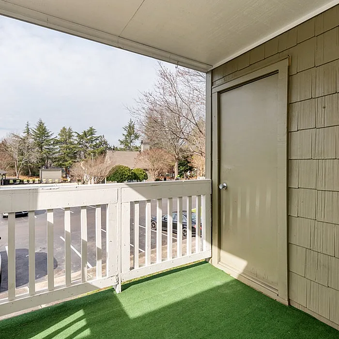 Charming apartment balcony with green artificial grass and scenic view of trees and open sky.