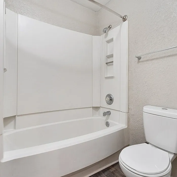 Modern bathroom featuring a pristine white bathtub with built-in shelves, sleek shower fixtures, and a contemporary toilet, offering a clean and inviting space.