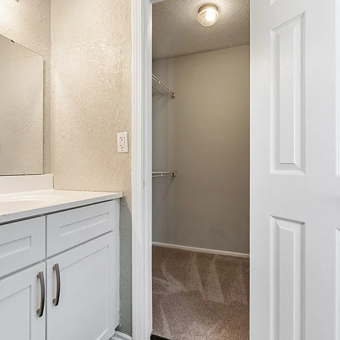 Elegant modern bathroom with sleek white vanity leading to a spacious walk-in closet.