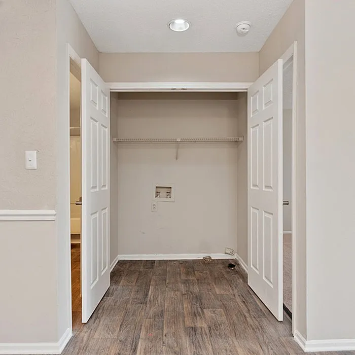 Charming laundry nook with double doors, featuring stylish wood flooring and ample shelving space.