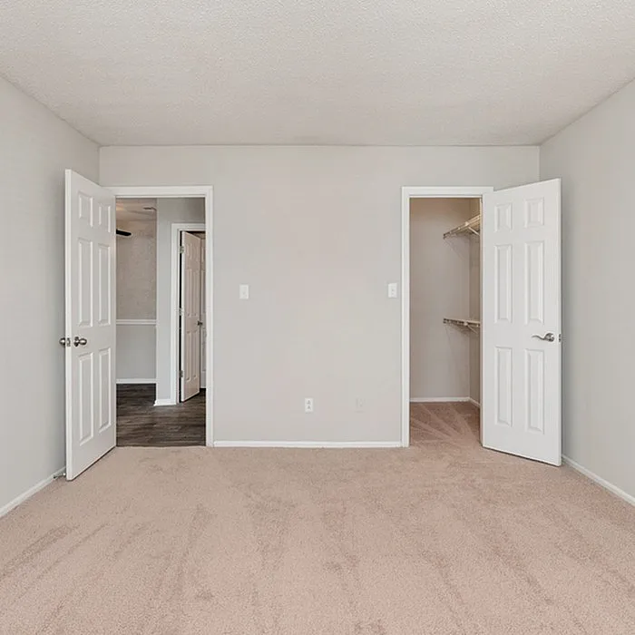 Bright bedroom with plush carpeting, featuring dual doors leading to a spacious walk-in closet and adjacent room, highlighting ample storage and versatile layout.