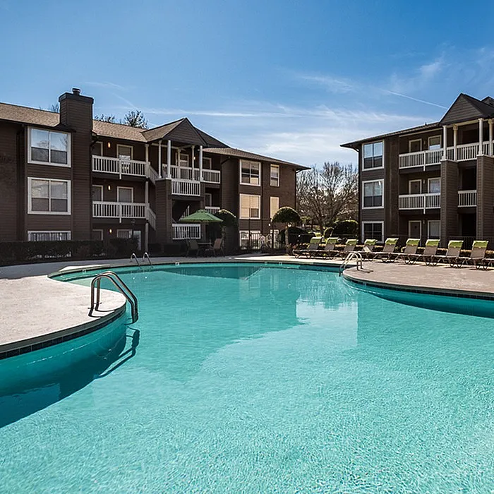 Inviting apartment complex with a sparkling outdoor pool, surrounded by modern architecture and poolside lounge chairs under a clear blue sky.