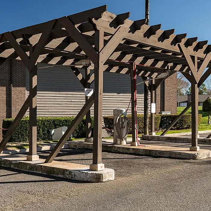Charming rustic pergola over a parking area with vibrant greenery and clear blue skies.