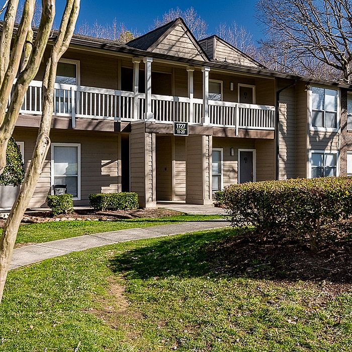 Charming two-story apartment building with private balconies, surrounded by lush greenery and well-maintained landscaping.
