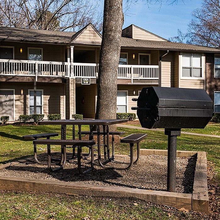 Charming apartment community with a welcoming picnic area and barbecue grill, surrounded by lush greenery.