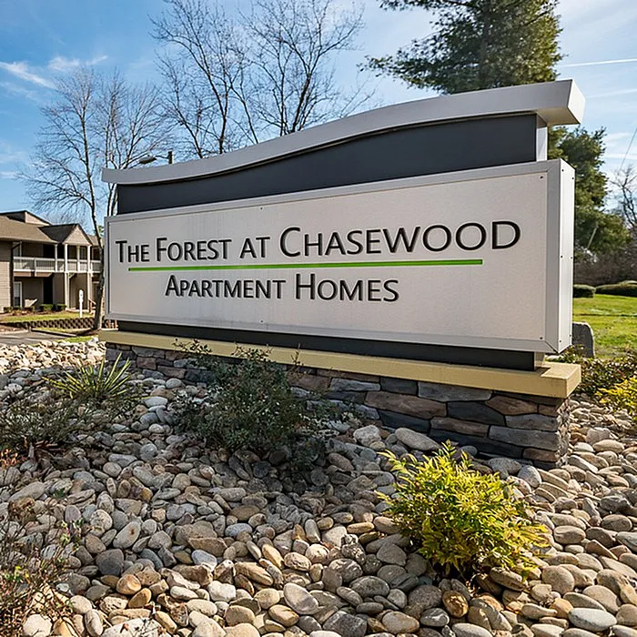 Inviting entrance sign for The Forest at Chasewood Apartment Homes surrounded by lush landscaping and serene stone accents.