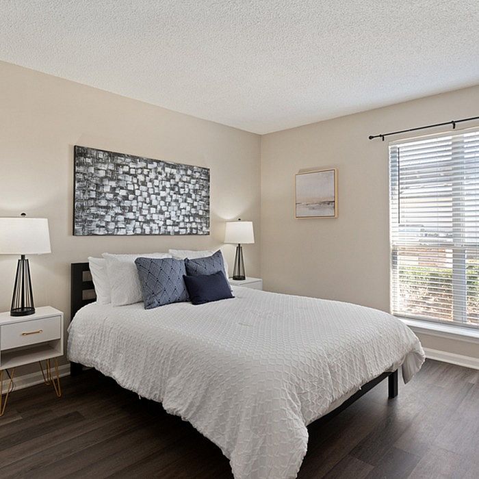 Bright and inviting bedroom with sleek hardwood floors, a cozy bed adorned with plush pillows, and abundant natural light streaming through large windows.