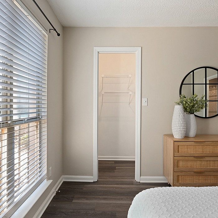 Bright bedroom with modern decor, featuring large windows, a stylish dresser with decorative vase, and a practical walk-in closet.