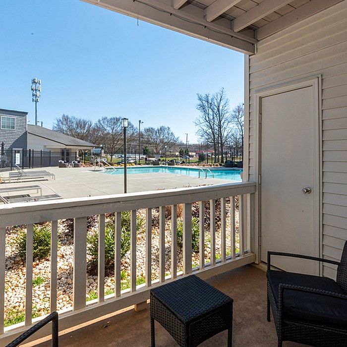 Inviting apartment balcony with cozy seating overlooking a refreshing swimming pool and sunlit courtyard.