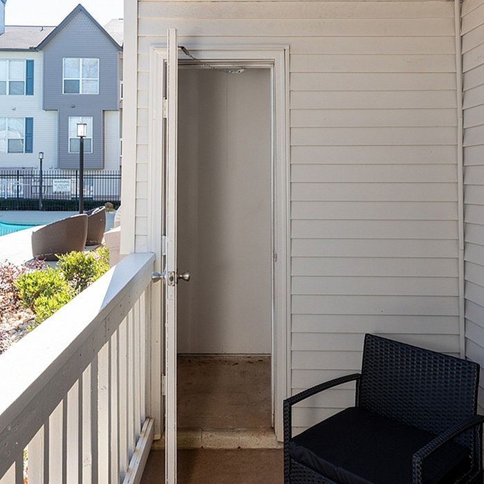 Charming patio with white siding and cozy seating, overlooking a lush garden and sparkling swimming pool.