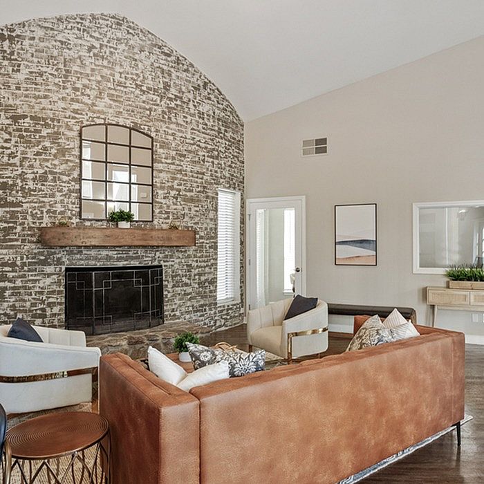 Chic living room with a rustic brick accent wall, stylish leather sofa, and plush armchairs surrounding a cozy fireplace.