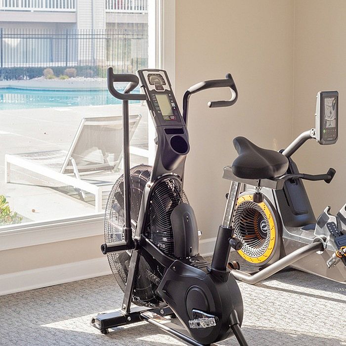 Modern apartment gym featuring state-of-the-art exercise bikes with a scenic pool view through large windows.
