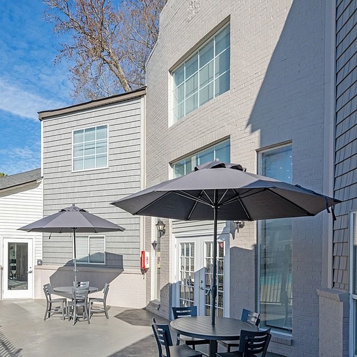 Charming patio area with elegant outdoor seating and modern sun umbrellas, set against a stylish building facade with large windows.